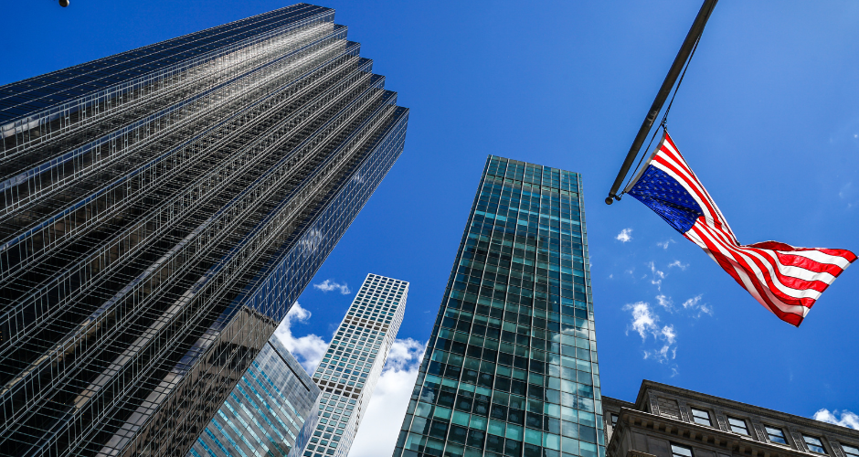 american flag and buildings in a point of view of looking up into the sky.